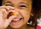 Child holding a small orange object near their eye